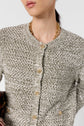 A woman wearing a textured, woven gray and white gilet coton chiné with gold buttons and a gold chain necklace. Only her lower face and upper torso are visible.