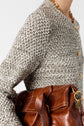 Close-up of a person wearing a textured gilet boutonné sweater with gold buttons and a gold chain necklace, holding a brown leather handbag with white stitching and gold hardware.
