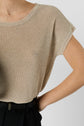 A person wearing a beige short-sleeve knit top tucked into high-waisted black pants, with one hand on their hip, against a plain light background.