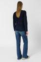 Person with long, straight hair wearing a navy sweater, blue jeans, and white shoes, standing with their back to the camera against a plain white background.