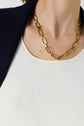 A close-up of a person wearing a gold chain necklace, a top en microfibre blanc ajusté, and a dark blazer. The focus is on the necklace and upper chest.