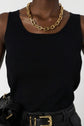 A person wearing a sleeveless black top, high-waisted black pants with a gold belt, and a chunky gold chain necklace. The image is cropped below the shoulders, focusing on the outfit details.