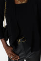 Person wearing a black top and jacket, paired with black leather pants and gold accessories including a necklace, belt, bag strap, and ring. The look is elevated with a gilet en microfibre noir for an added touch of sophistication. The photo is cropped to show only the torso and part of one arm.
