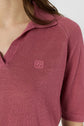 A person wearing a short-sleeved, dusty rose knit polo col ouvert shirt with a collar and a small embroidered logo on the left chest. Only the upper torso and part of the neck are visible.