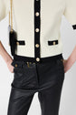 Person wearing a gilet chic white and black top with gold buttons, black leather pants, and a black shoulder bag with a gold chain strap. Only the torso and upper legs are visible.