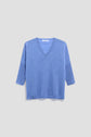 A light blue, long-sleeve cachemire pull femme with a col V is displayed on a plain, pale gray background. The sweater has a relaxed fit and ribbed cuffs and hem.