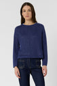 A woman stands against a plain white background wearing a pull bleu indigo, styled with dark blue jeans. The pull col rond in lightweight pull lin drapes comfortably as she looks straight at the camera with a neutral expression.