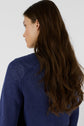A woman with long, wavy brown hair wearing a pull col rond bleu indigo is shown from the back and side, facing left against a plain white background.