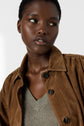 A person wearing a brown suede jacket over a textured pull lin femme col V top looks slightly to the side against a plain background.