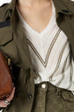 A person wearing an olive green jacket and high-waisted pants with a white pull rayé femme V-neck top featuring dark chevron stripes, holding a brown leather bag.