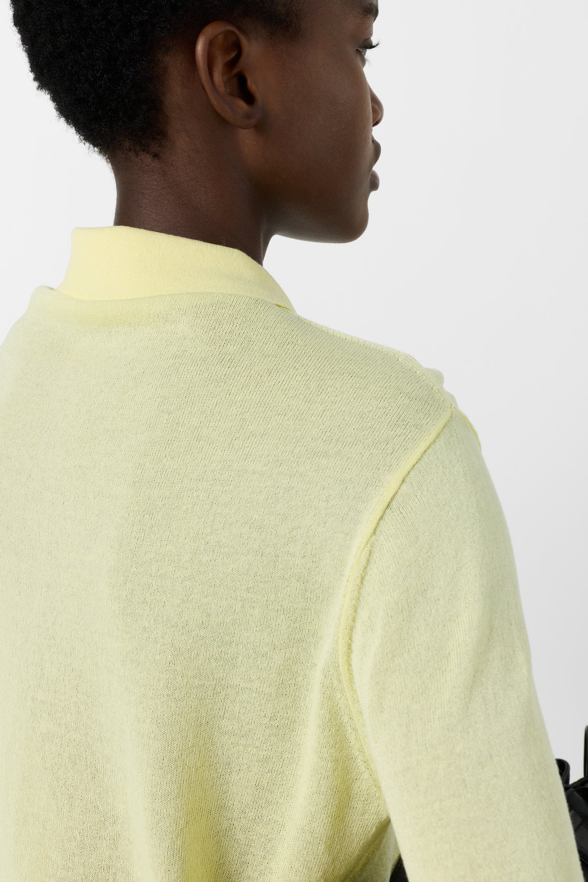 A person with short hair, seen from behind, wearing a light yellow collared sweater against a plain white background.