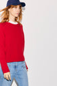 A person with long red hair wears a navy blue cap, an Esprit pull col rond rouge en laine over a white shirt, and blue jeans, walking against a plain white background.