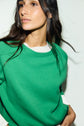 A woman with long dark hair wears an Esprit pull laine vert à col rond, layered over a white top, looking off to the side against a plain white background.