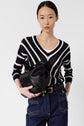Woman with straight black hair wears a pull rayé noir et blanc in coton, featuring subtle maille ajourée for a delicate touch. She pairs it with dark blue jeans with contrast stitching and holds a large black leather bag. She stands against a plain white background.