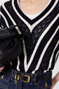 A person wearing a navy and white pull rayé V-neck sweater in coton with delicate maille ajourée details, high-waisted blue jeans, a black belt with a gold buckle, and holding a black leather bag.