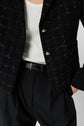 Person wearing a white ribbed tank top, a black plaid textured blazer with gold buttons—perfect as a veste noire carreaux or veste chic femme—and black pleated pants with a black belt. Only the torso and part of the arm are visible.