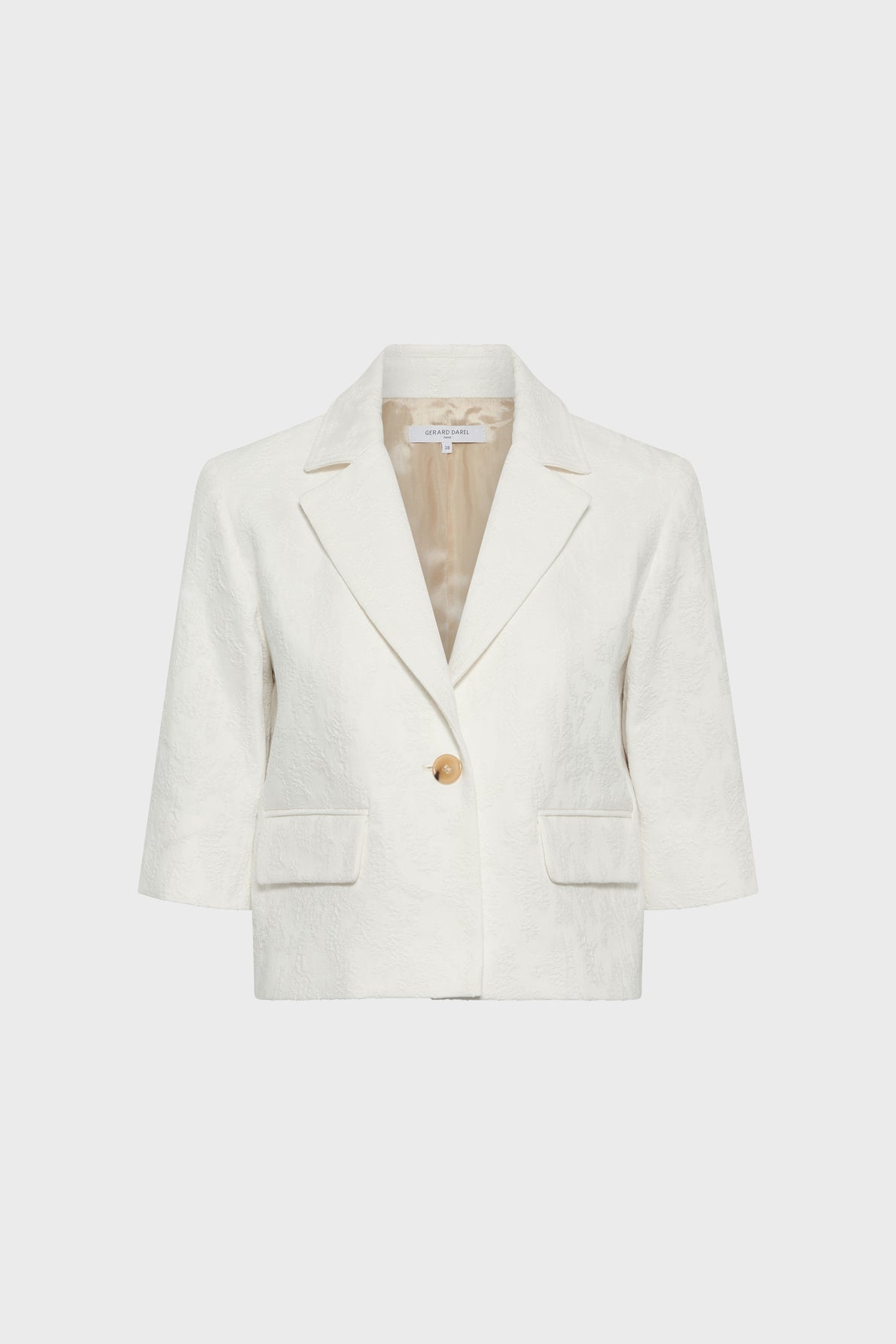 Cropped white veste courte with a subtle motif jacquard pattern, notched lapels, three-quarter sleeves, two front flap pockets, and a single gold button closure, displayed on a plain light background.