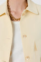 A close-up of a person wearing a crème-colored veste courte jacket over a white shirt, accessorized with a chunky gold chain necklace.