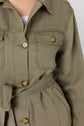 Close-up of a person wearing a veste kaki button-up jacket with a tied waist belt, large buttons, and flap chest pockets over a white top. The person’s face is not visible.