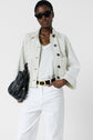 A person wearing sunglasses, a veste rayée femme over a white shirt, white pants, and a black belt, holding a black bag. They also wear a chunky gold necklace.