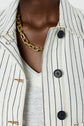 A person wearing a white pinstriped jacket with black buttons, styled as a veste rayée femme, paired with a white top and a gold chain necklace.