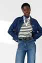A person wearing a veste courte en denim, striped polo shirt, and high-waisted jeans with front pockets stands with hands on hips, looking at the camera.
