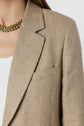A close-up of a person wearing a beige blazer over a white ribbed top, with a gold chain necklace. The background is plain white.