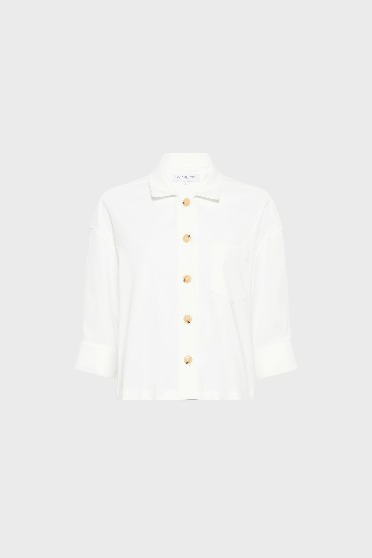 White long-sleeve button-up shirt with a collar, front pocket, and large gold buttons, displayed against a plain light gray background.