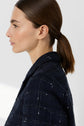 Woman with straight brown hair in a low ponytail, wearing a dark textured jacket, shown in profile against a plain light background.