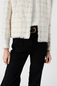 A person wearing a white plaid textured veste écru, white top, black pants, and a black belt with a gold buckle. Only the torso and upper legs are visible.