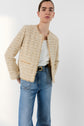 A person wearing a cream veste tweed femme courte over a white top and blue jeans with a black belt, standing against a plain white background.