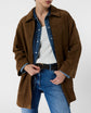 Person wearing a brown suede jacket over a denim shirt, white T-shirt, blue jeans, and a black belt, standing against a plain white background. Their face is partially out of frame.