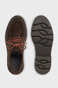A pair of brown derby cuir velours shoes is shown from above and below; one displays the top with orange-brown laces, highlighting the style of a chaussure lacée, while the other reveals the textured rubber sole with a wavy semelle crantée tread pattern.