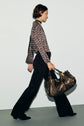 A person wearing a blouse Lorra with un imprimé graphique and black pants walks while carrying a large brown leather bag.