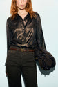 A woman with red hair wears a chemise satinée noire and dark pants, holding a dark brown bag at her side. Only her upper body is visible against a light background.