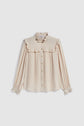 Cream-colored long-sleeve blouse with ruffled collar, shoulders, and cuffs, reminiscent of a chic chemise à volants. Button-down front with a loose fit and soft, lightweight fabric in the style of a classic chemise soie, displayed on a plain white background.