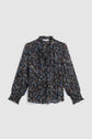 Long-sleeve chemise à fleurs with a col volanté and cuffs, featuring a dark floral pattern in blue, brown, and beige tones. Crafted from mousseline soie for a delicate finish, this blouse has a loose fit and is displayed on a plain, light background.