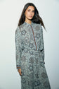 Woman with long brown hair wearing a chemise fluide femme and matching skirt in an élégant imprimé floral, standing against a plain white background, looking at the camera with a neutral expression.