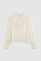 A long-sleeve, off-white chemise en crêpe with lace trim on the cuffs and a delicate col volanté, featuring a round yoke, manches bouffantes, and a loose fit.
