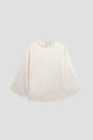 Cream-colored, long-sleeve top satiné écru with a round neckline and a delicate col perlé doré, featuring a button closure at the back, displayed flat on a light gray background.