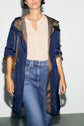 A woman wearing a beige blouse, blue high-waisted jeans, and a navy parka femme à capuche mi-longue with rolled-up sleeves stands against a plain light background.