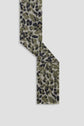 A narrow écharpe léopard with an olive green, black, and beige leopard print pattern is laid out in a zigzag shape on a plain light gray background.