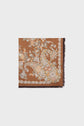 A brown square scarf with an ornate paisley and motif fleuri pattern in beige, cream, and orange tones. The scarf features subtle franges along the edge, showcasing the refined elegance of an étole soie.