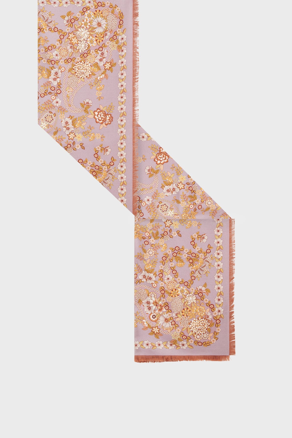 A rectangular étole soie with fringed edges, featuring a motif fleuri in shades of gold, pink, and white on a pale lavender background, displayed against a plain light backdrop. This foulard bohème brings an elegant touch to any ensemble.