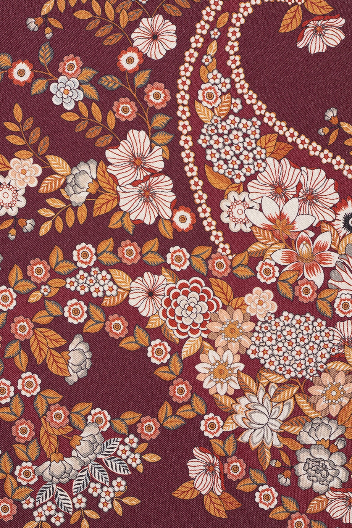 Patterned fabric with a red background, decorated with an intricate motif fleuri in white, orange, yellow, and beige—featuring leaves and clusters of small flowers in a winding, symmetrical arrangement reminiscent of a foulard bohème.