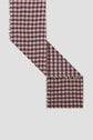 A piece of fabric with a red, black, and beige motif à carreaux, slightly frayed edges, arranged at an angle against a plain white background.