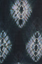 Dark fabric with a tie-dye pattern featuring repeating diamond shapes in white and blue, each containing a black abstract design, creates a symmetrical and textured appearance—perfect for an écharpe tie and dye that adds a unique touch to your style.