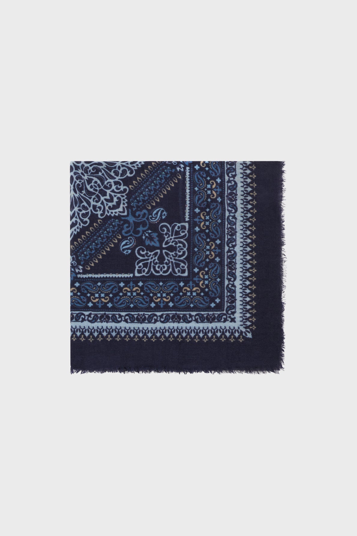 A navy blue carré en laine square scarf with light blue and white intricate floral and paisley patterns, motif bandana details, and frayed edges.