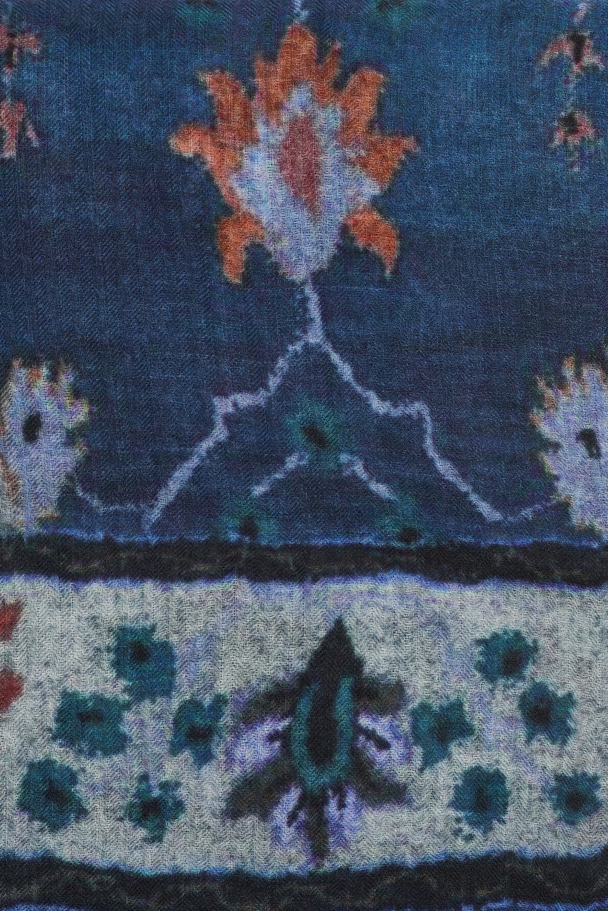 Close-up of an echarpe bleue, showcasing a blue fabric with a motif fleuri featuring stylized orange and teal floral motifs arranged in rows, separated by a thin black horizontal line, against a textured background.