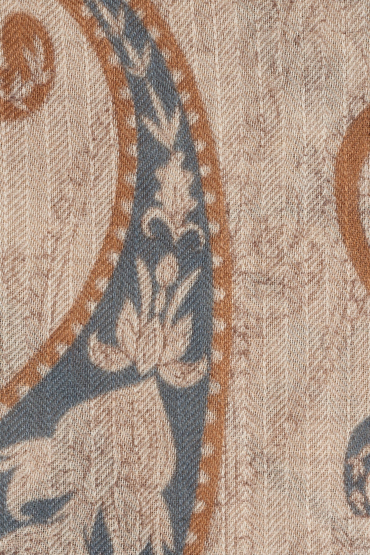 A close-up of a woven fabric with a floral and paisley pattern in blue, tan, and beige tones, featuring textured details and intricate designs reminiscent of an écharpe motif cachemire.